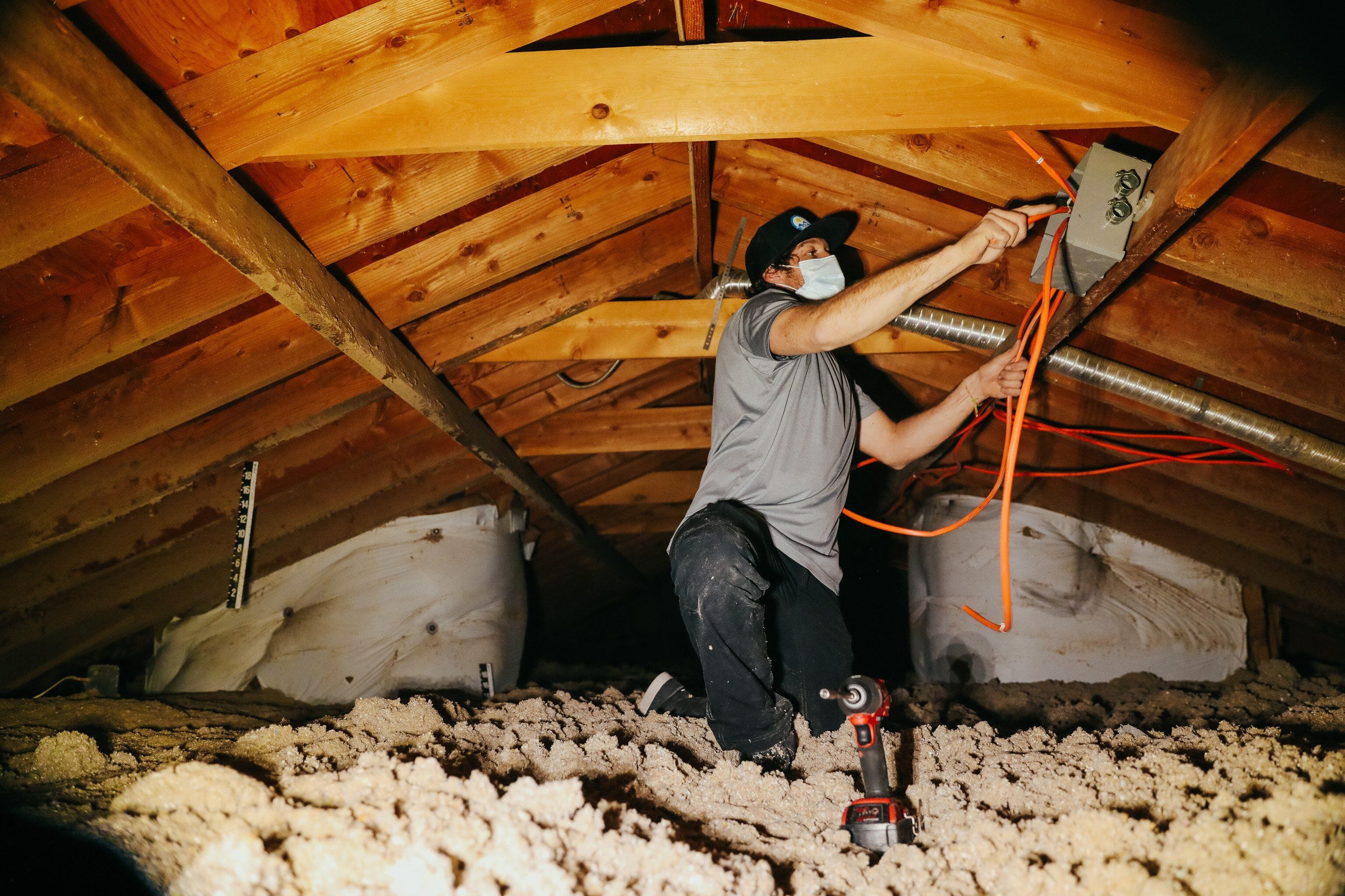 An electrician with Elevated Independent Energy wears Truewerk workwear as he completes an attic's solar wiring installation.