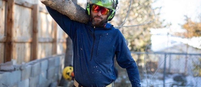 A male trade professional carries a log over his shoulder as he wears a blue Truewerk work shirt, which makes a great gift.