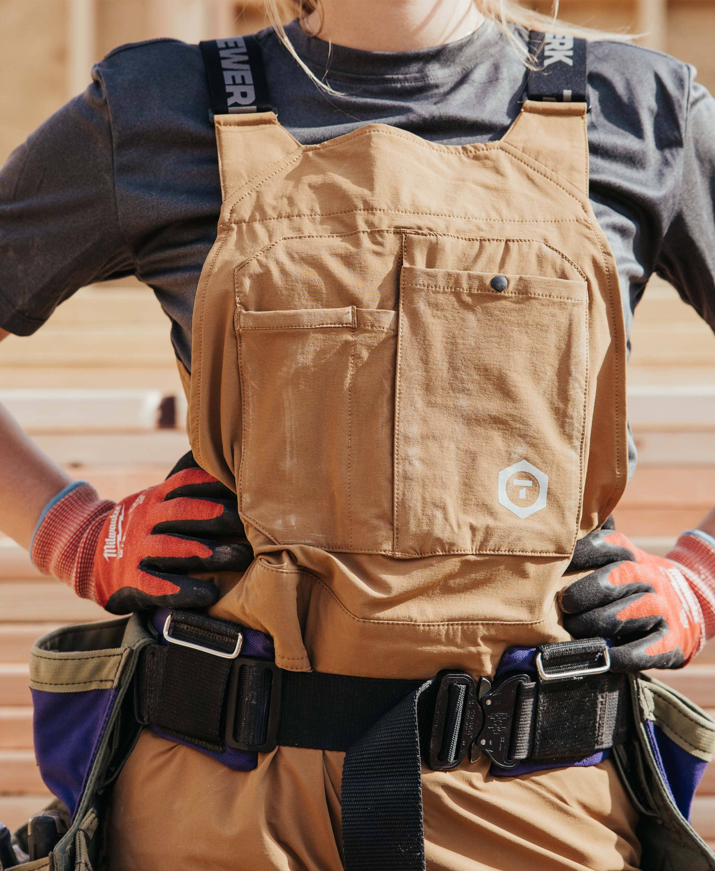 A female trade professional wears a women's fit green vis T.5 WerkHoody by Truewerk while holding a drill as she works.