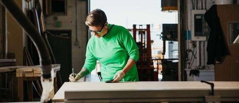 Trade professional Sonne Shields wears a green vis Truewerk WerkHoody as she marks cutting points with a pencil.
