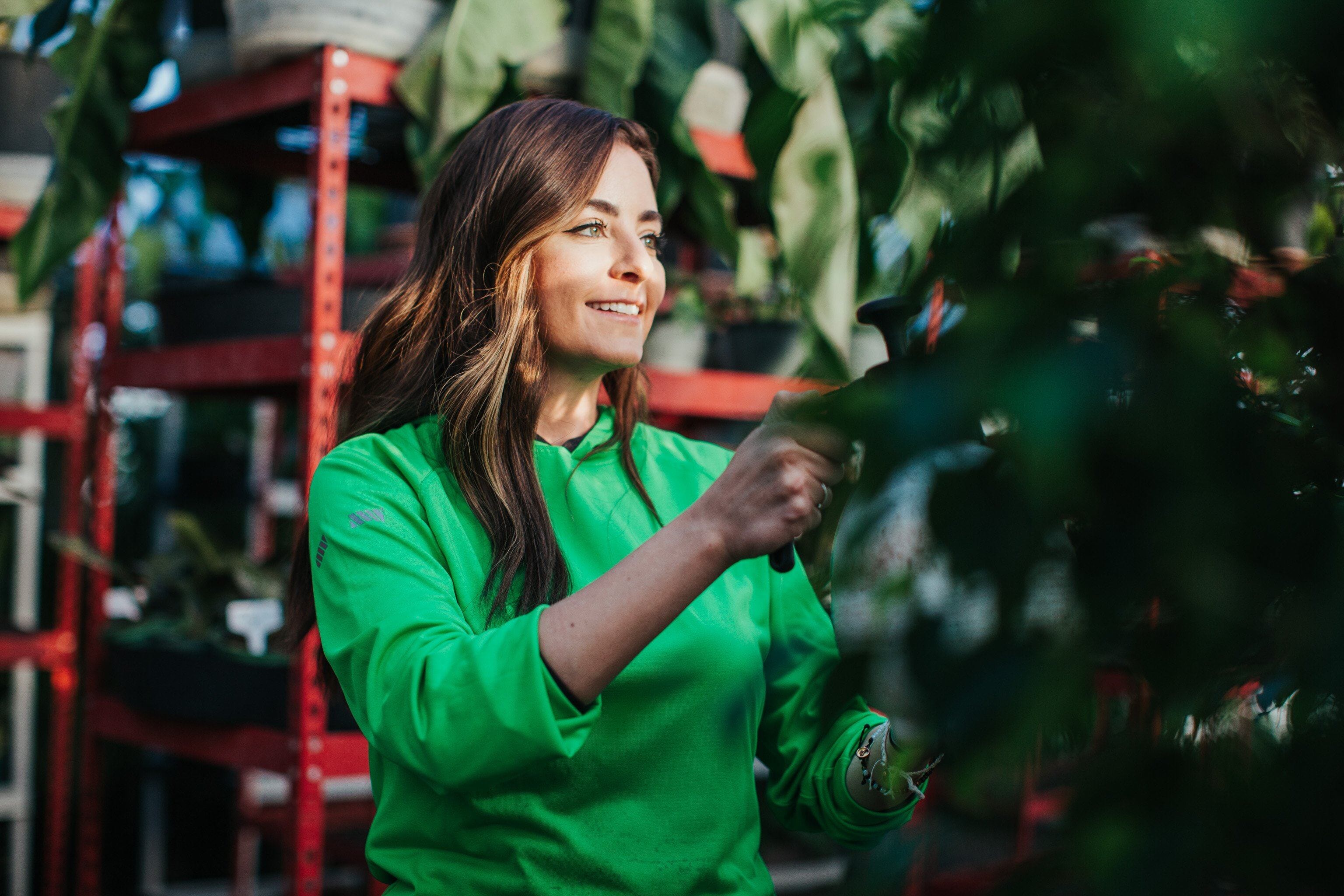 A plant nursery professional wears a green vis Truewerk WerkHoody as she tends to the plants with a pair of shears.