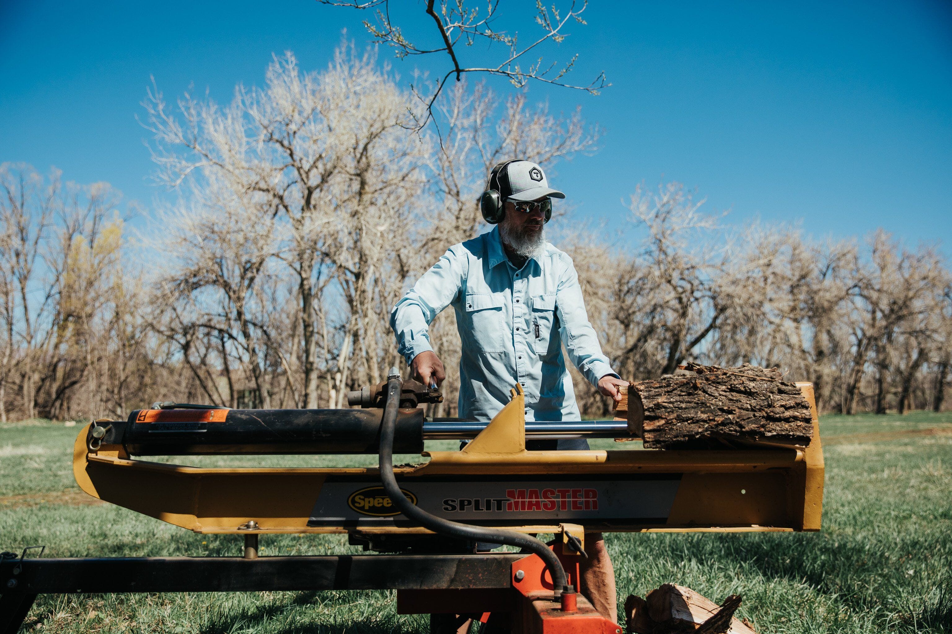 A trade professional wearing a blue Truewerk cloud shirt and hat stands by a piece of industrial woodcutting equipment.
