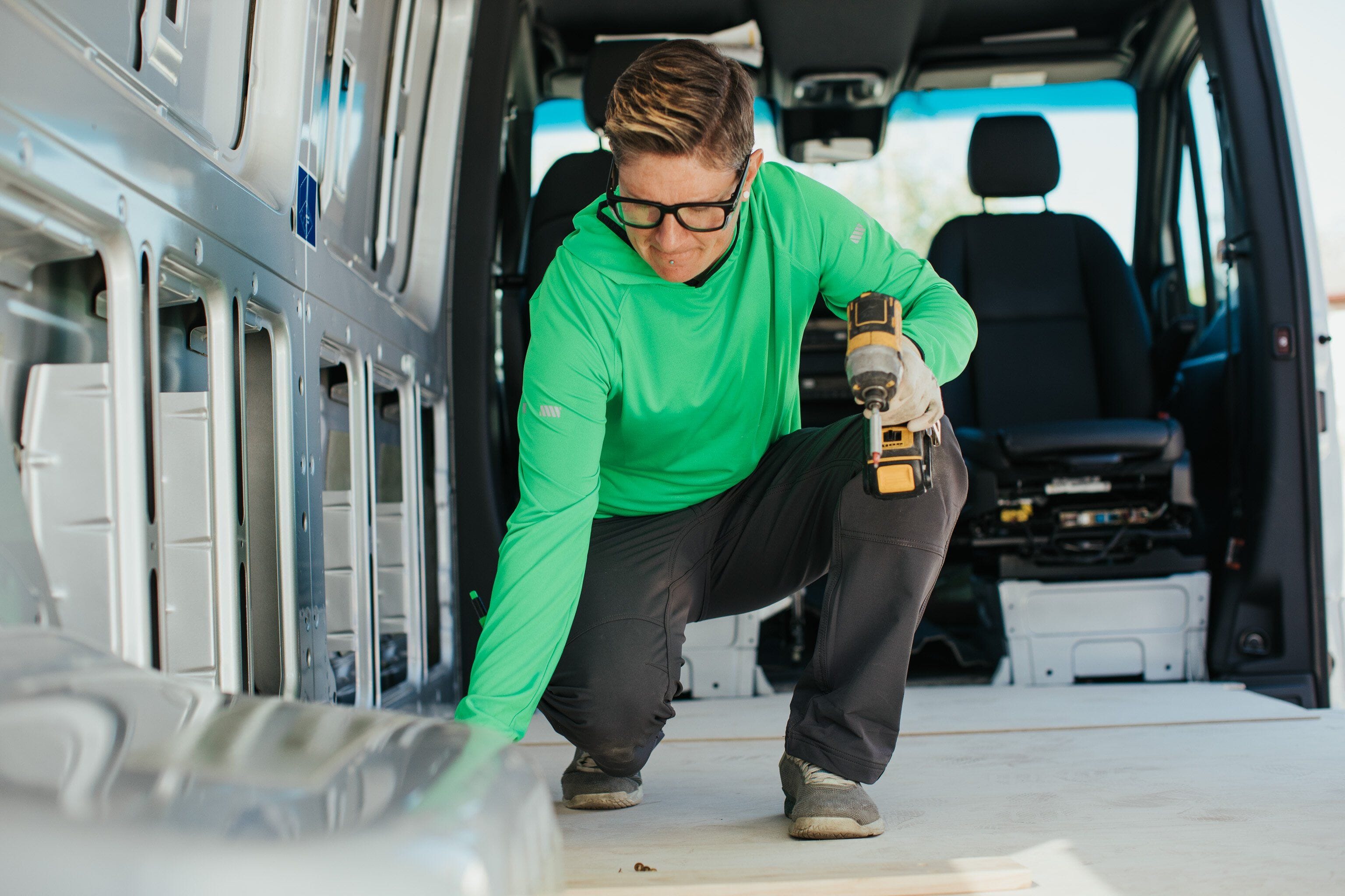 A female trade professional wears a women's fit green vis T.5 WerkHoody by Truewerk while holding a drill as she works.