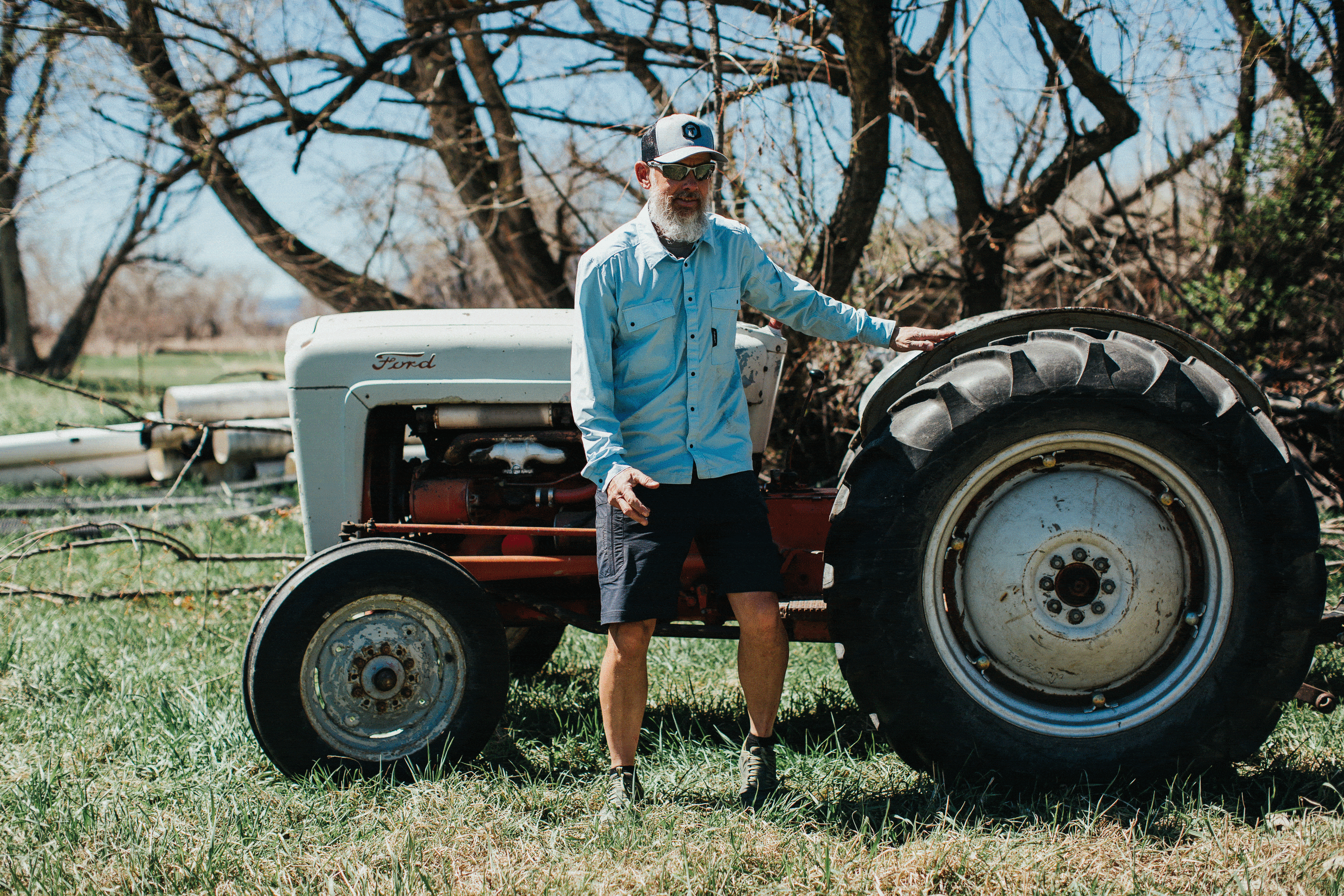 A retired male trade professional wearing Truewerk workwear shorts stands in front of a vintage Ford tractor.