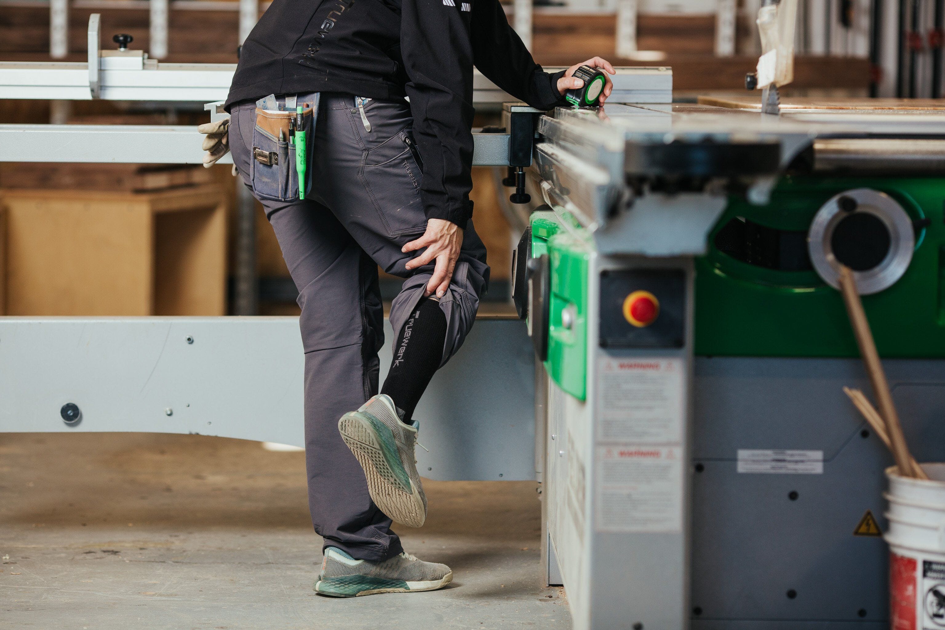 A trade professional in a machine shop wears gray Truewerk WerkPants and black Truewerk workwear socks.