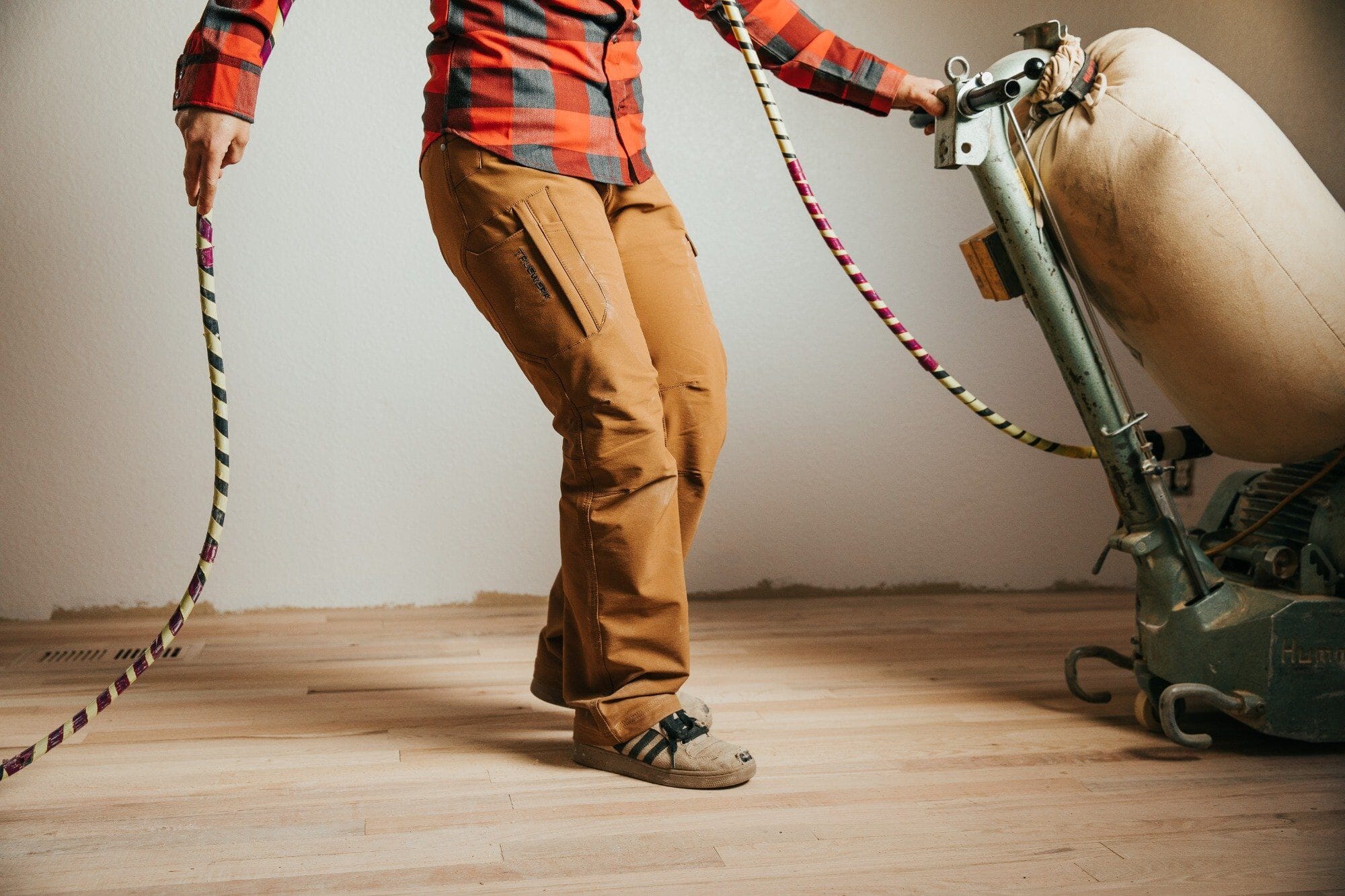 A home renovation contractor wearing Truewerk flannel and WerkPants pushes a buffer over a hardwood floor.