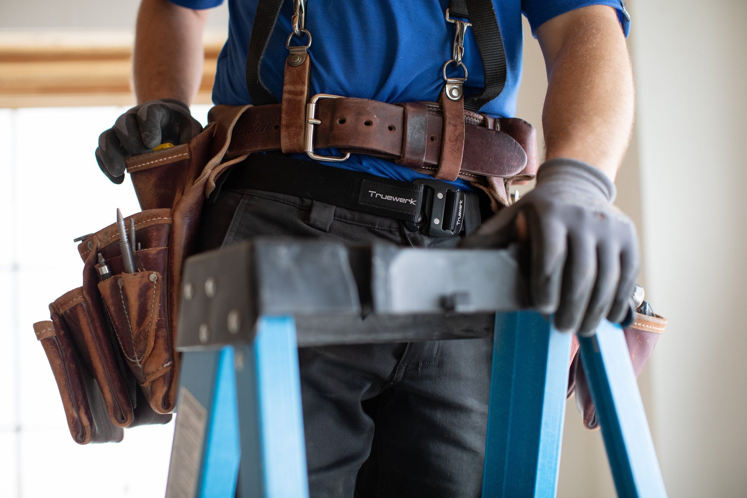 A male construction professional wears gray Truewerk WerkPants, a Truewerk belt, and a harness as he prepares to work on a stand.