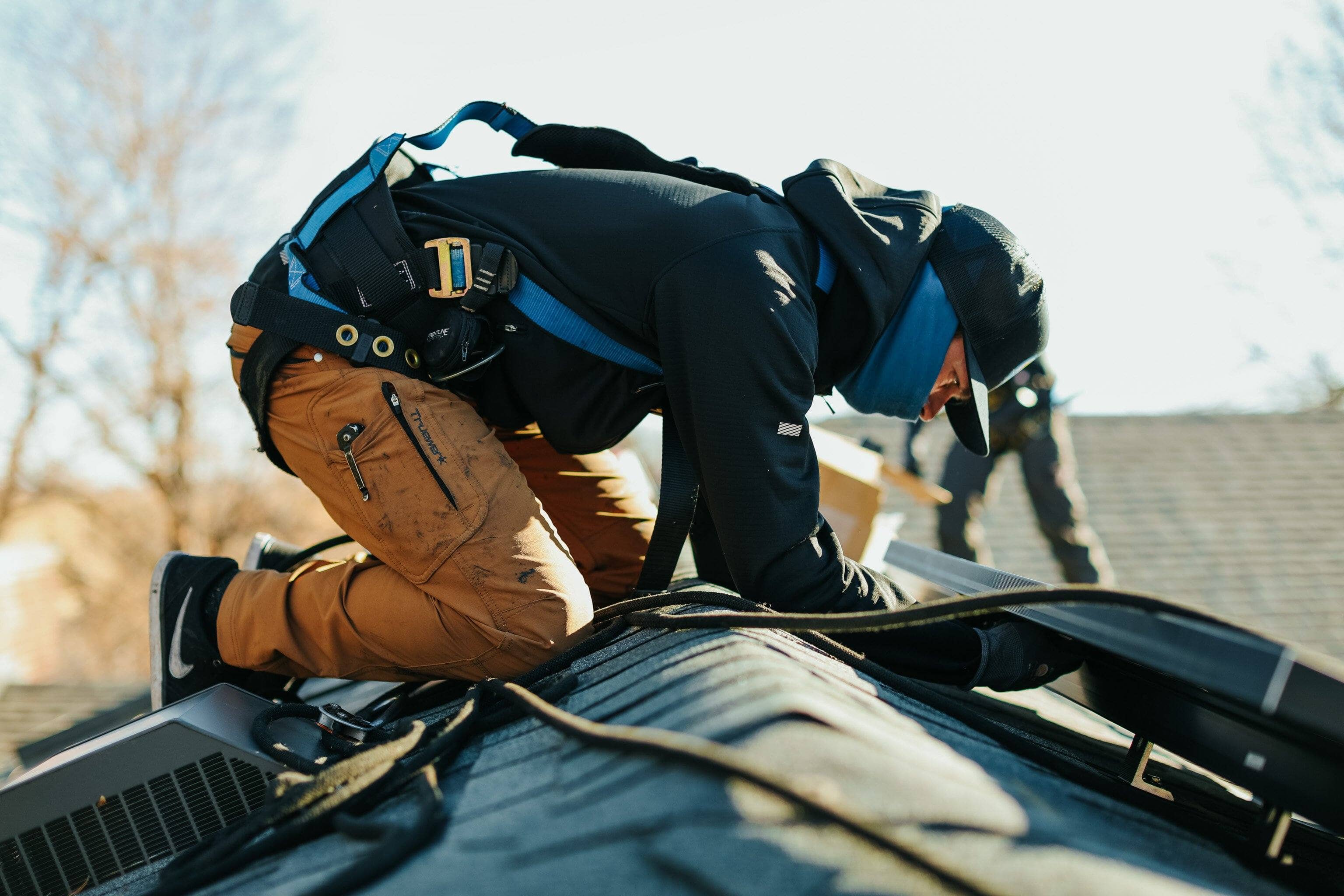 A roofer wears brown Truewerk WerkPants in cold weather as he installs solar power panels on the top of a home roof.