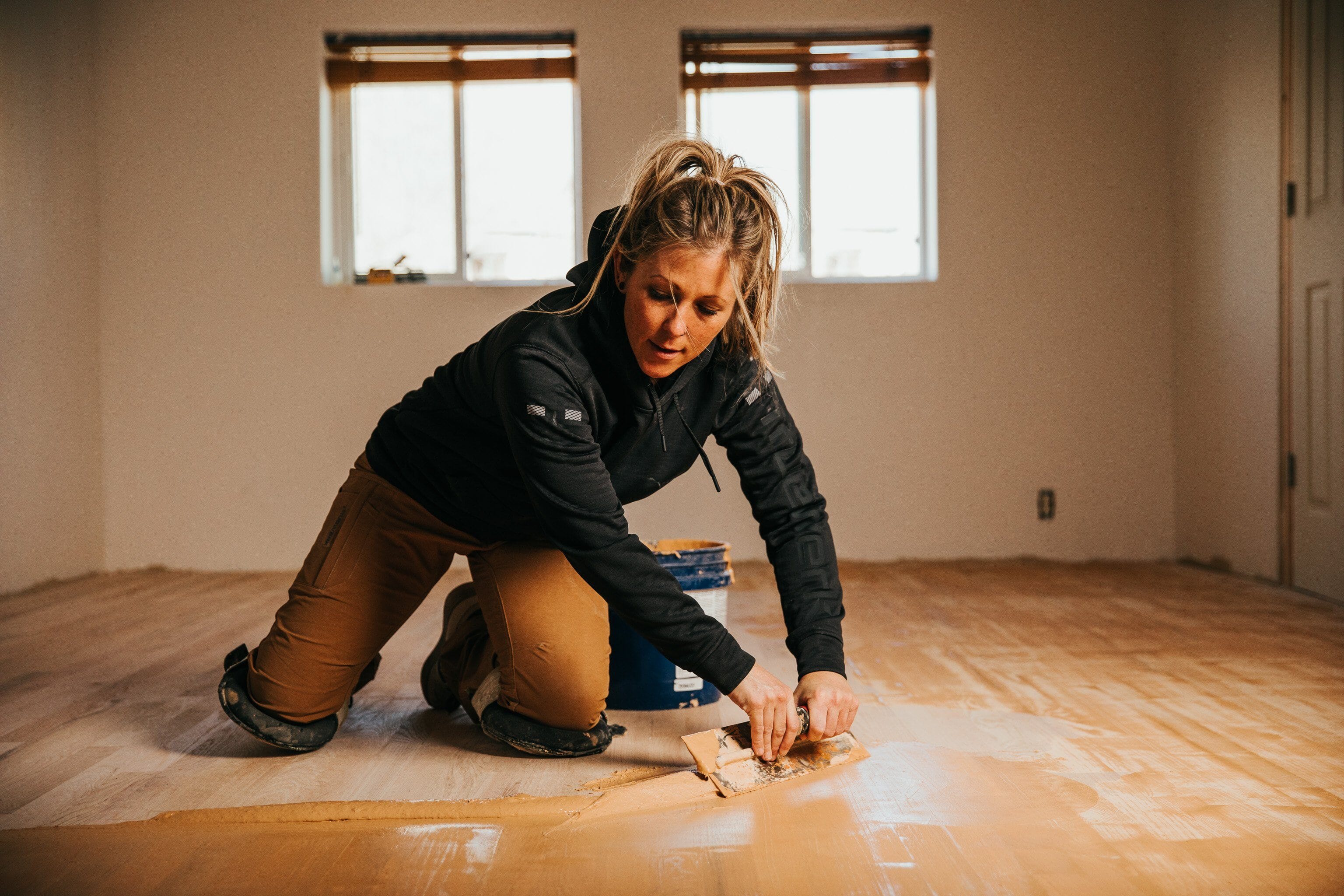 An industrial athlete wears brown Truewerk WerkPants as she rehabilitates a hardwood floor during a home remodel.