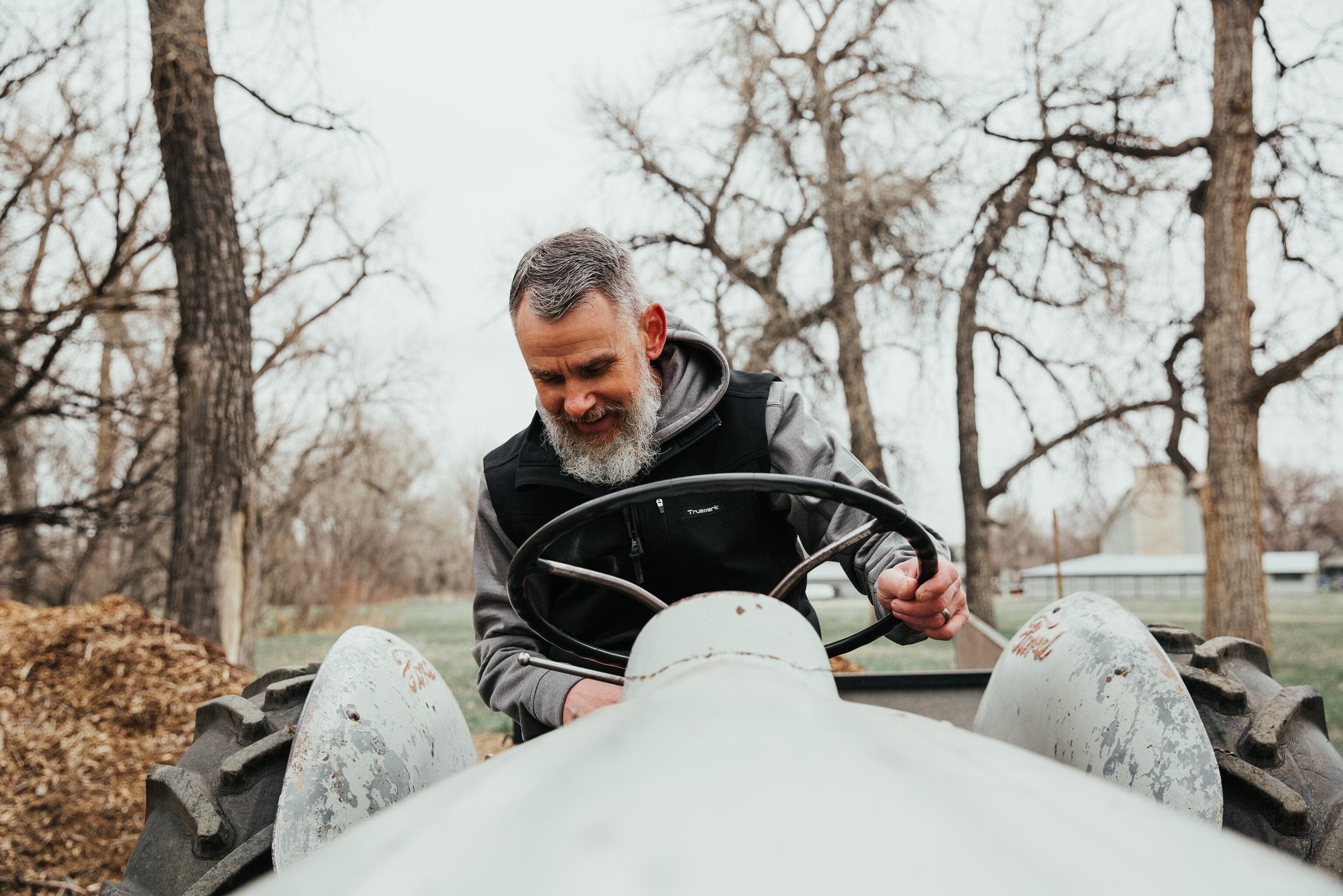 An industrial athlete wears a Truewerk workwear vest as he sits on a vintage blue Ford tractor.